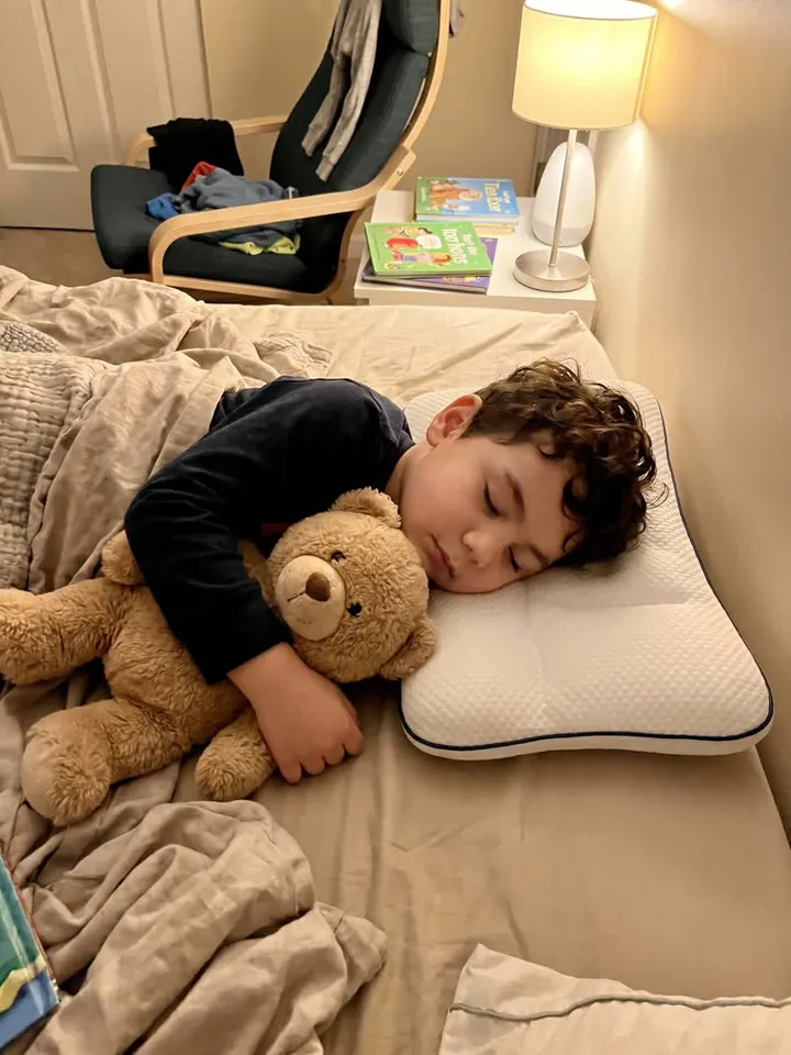 Boy asleep with a teddy bear, his head resting on the LittleBear pillow